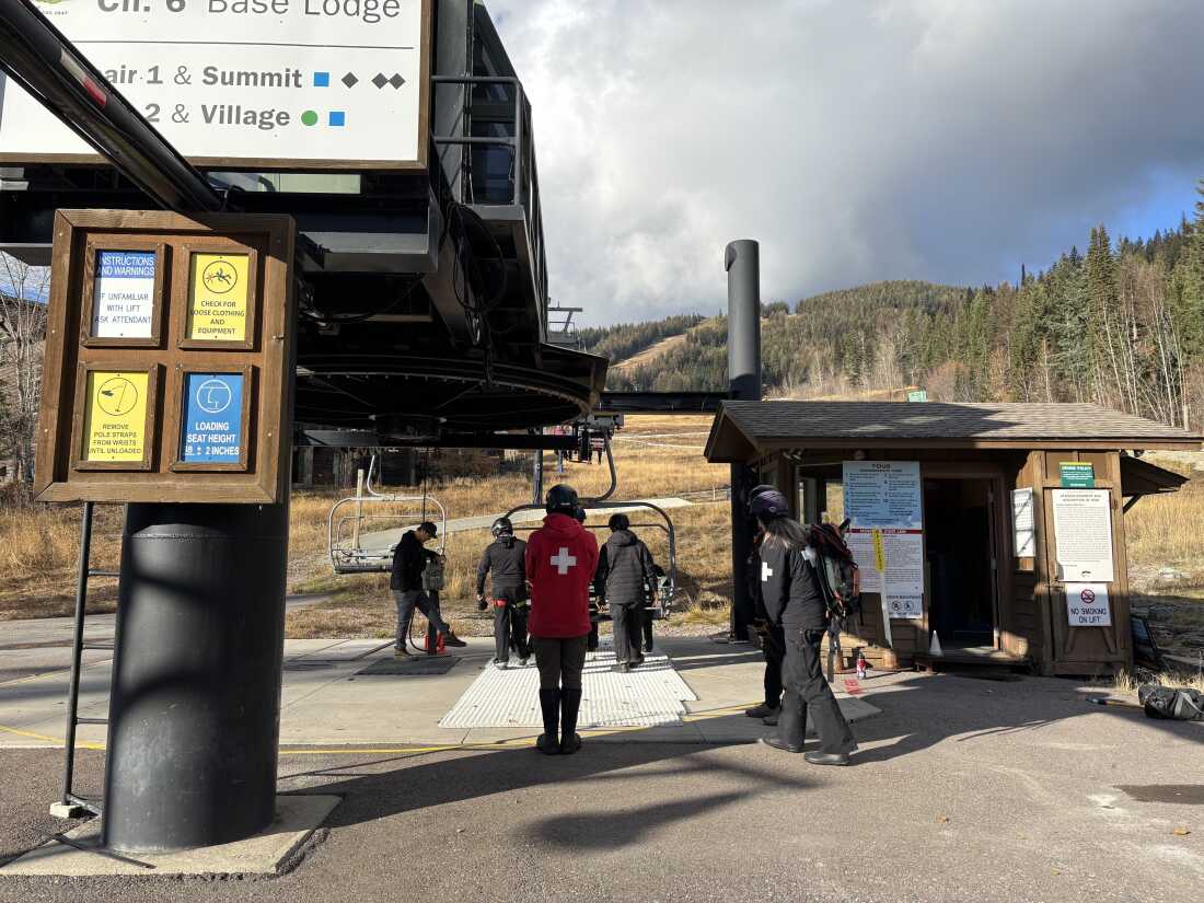 Ski patrollers at the Whitefish Mountain Resort in Montana conduct preseason trainings on November 19. They stand near a chairlift. Conifer trees rise up in the background.