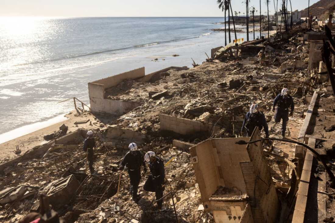Members of of a search and rescue team comb through the ruins of a burned home.