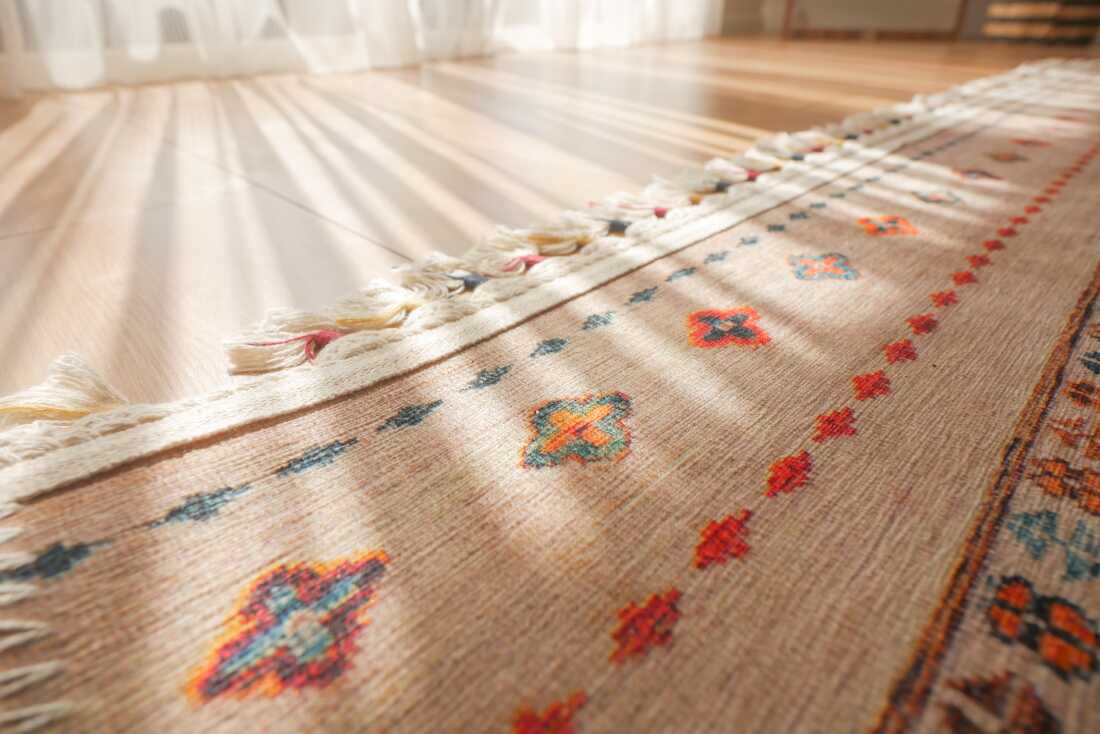 A close-up, low-angle photograph of an area rug on a wood floor with light pouring in fron an adjacent window. 