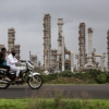 Reliance Industries' oil refinery in Jamnagar, India, is a network of metal towers, pipes and tanks in this photo. In the foreground, two men ride a motorbike on a road.