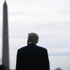 This photo shows President Trump standing outdoors with his back to the camera. The Washington Monument rises in the background.