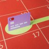An illustration made of cut paper shows a purple credit card standing up on a flat, red calendar with dates numbered in the grid. A green circle below the card turns into a line that stretches out into the future, demonstrating making a plan to pay off credit card debt.