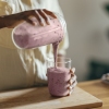 Close-up of woman pouring a meal replacement shake into her friend's glass. Horizontal shot.