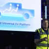 Wearing a fluorescent yellow safety vest, Ford CEO Jim Farley speaks at the Louisville Assembly Plant, in Louisville, Kentucky, on August 11, 2025. Behind him is a large screen with a graphic of a pickup truck and the words "Ford Universal EV Platform."