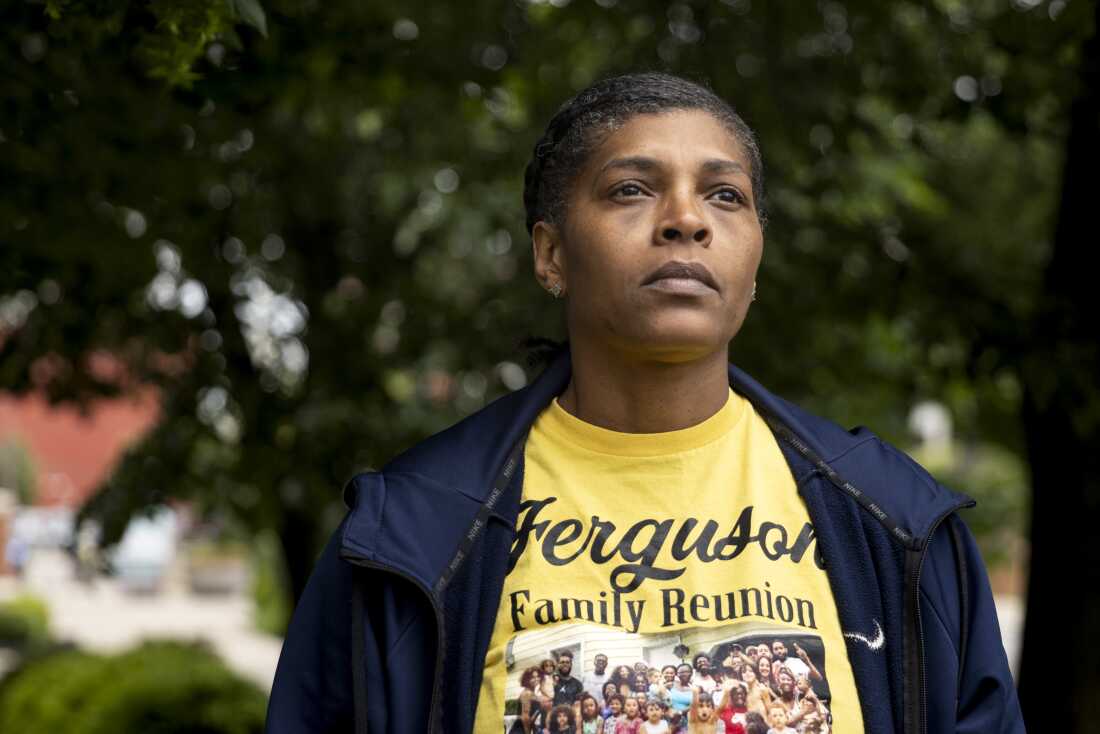 A portrait of Tyeesha Ferguson. She has a resolute look on her face and she is wearing a yellow t-shirt that says "Ferguson Family Reunion."