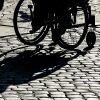 A person in a wheelchair casts a shadow on a cobblestone road. 