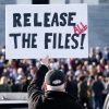 A protester with his back to the camera outside the U.S. Capitol holds a sign that says "release all the files!" 