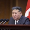 North Korea's leader sits behind a row of microphones with a North Korean flag behind him.
