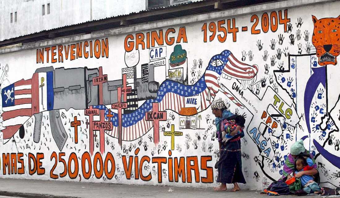 Indigenous women beg in Guatemala in June 2004 in front of a propaganda mural that speaks against U.S. interventions in the region.