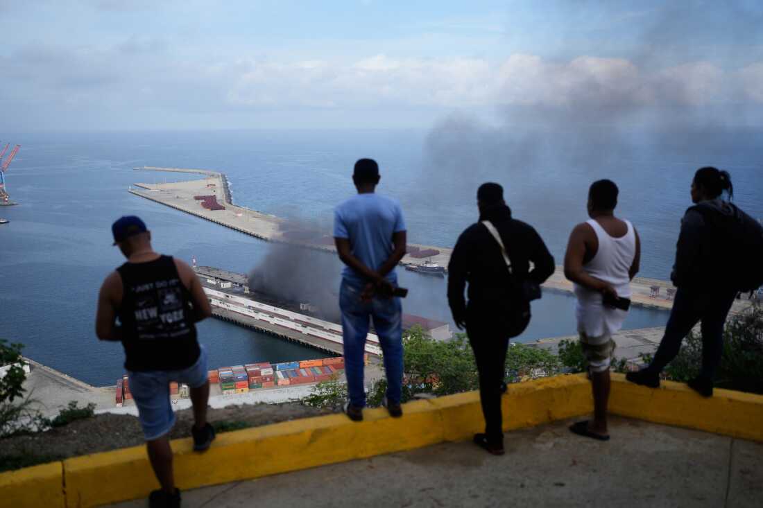 Men watch smoke rising from a dock after explosions were heard at La Guaira port, Venezuela.