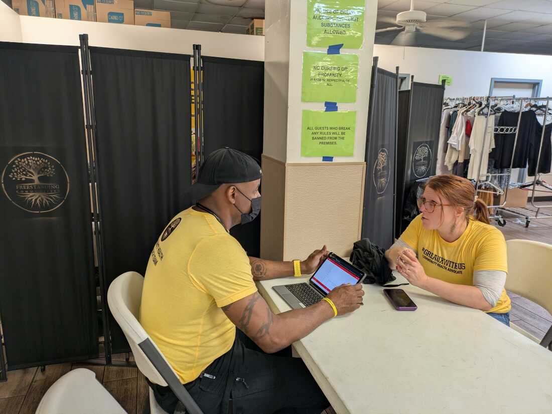 Dr. Elyse Stevens and her husband, Aquil Bey sit across a table from each other. Bey is looking at a tablet computer. They are wearing matching yellow t-shirts.
