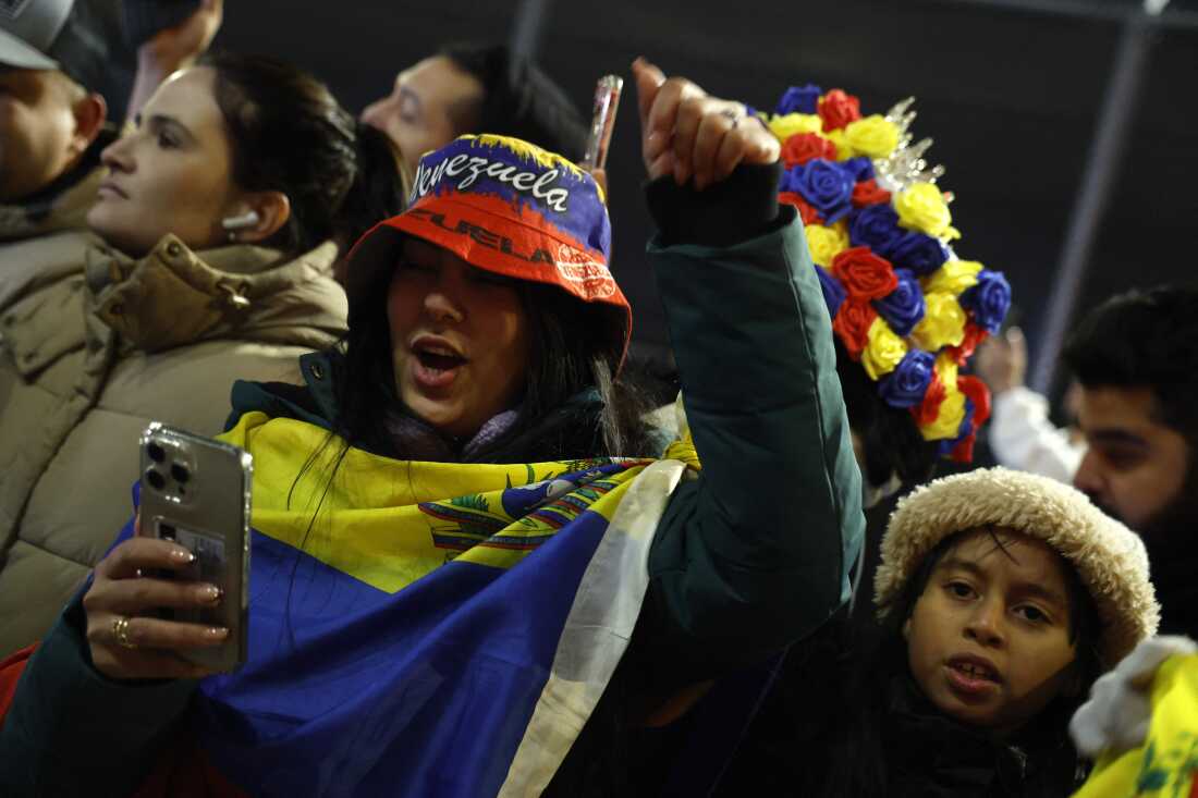 A woman standing among a crowd of people wears the Venezuelan flag draped across her chest and shoulders as they all celebrate outside the Metropolitan Detention Center in Brooklyn, New York.