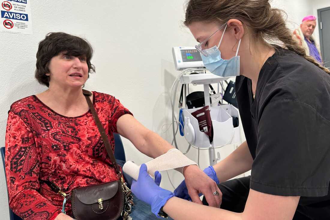 In this photo, MVP shelter resident Jamie Mangum is seated in a chair with her left arm extended out, while emergency medical technician Emily Woolsey wraps Mangum's wrist.