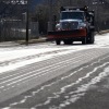 A truck with a snowplow on the front applies salt brine to a road.