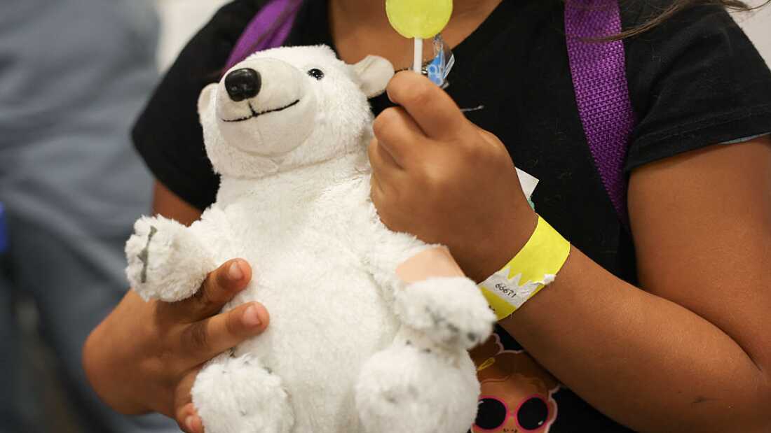 A child holds a toy bear with a band-aid after receiving a flu shot during an immunization event in Los Angeles. Flu is one of six vaccines that will no longer be given routinely but now require a consultation with a doctor.
