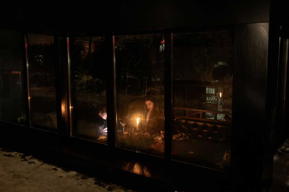 TOPSHOT - People sit in a dimly lit bar by candlelight during a power outage in Kyiv, on January 22, 2026, following Russian missile and drone attacks on Ukrainian energy infrastructure amid the Russian invasion in Ukraine. (Photo by Roman PILIPEY / AFP via Getty Images)