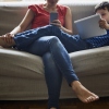 A mother and son relax on a sofa while using a smartphone and a digital tablet, respectively.