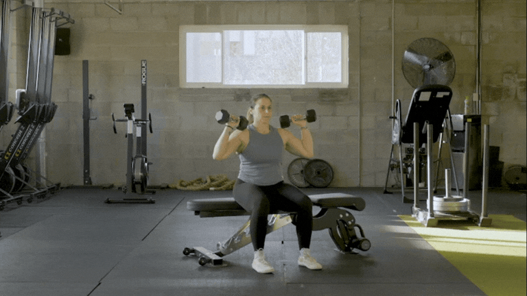 Sit on a bench, holding dumbbells by your shoulders. Push them both overhead, keeping your elbows close to your ears and your wrists stacked over your shoulders. With control, lower your arms back to your shoulders.