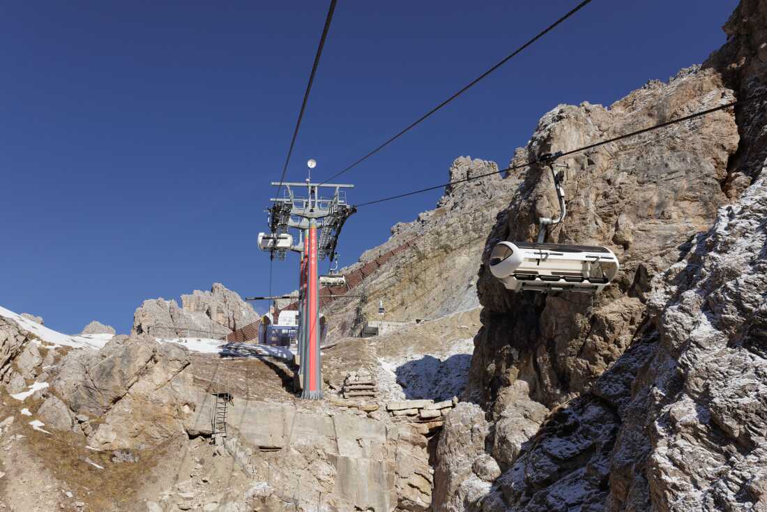The Prada logo is prominently displayed on a pylon of the Tre Croci - Son Forca chairlift, which stands over noticeably thin snow cover on the slopes of the Cristallo massif. This image captures two major challenges facing the Milano Cortina 2026 Winter Olympics: the increasing reliance on private luxury investment to fund infrastructure and the stark reality of climate change in the Dolomites. As temperatures rise, the scarcity of natural snow forces a greater dependence on artificial snowmaking, a process that environmental activists argue is unsustainable due to its high energy and water consumption